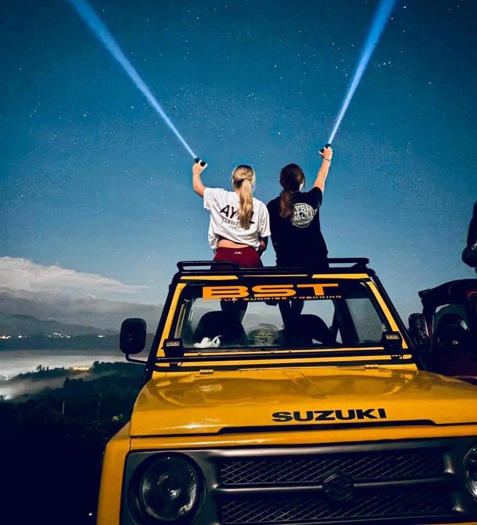 Group of friends on a vintage 4WD open jeep watching sunrise above the clouds in Mount Batur Bali
